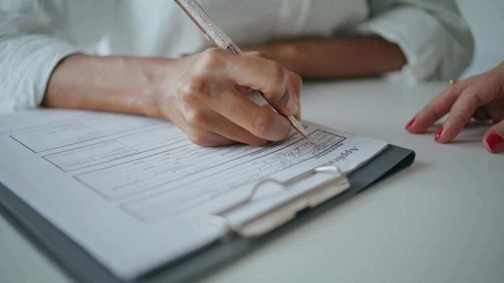 Closeup hands writing application papers on desk. Patient signing insurance form