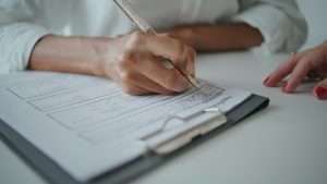 Closeup hands writing application papers on desk. Patient signing insurance form