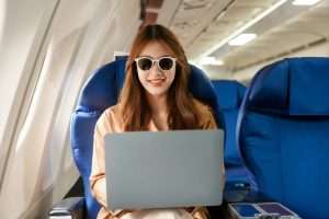 An Asian woman travels abroad by plane,sitting window. She listens music while flying, looks phone