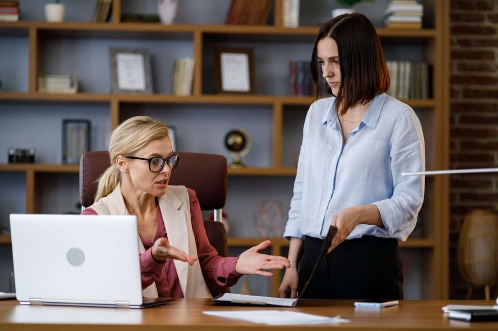 Angry female boss scolding sad and scared office worker. Demanding manager leader is annoyed at