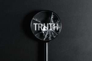 Broken magnifying glass focused on word Truth on black background, top view. Creative concept
