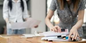 Businesswoman hands working in Stacks of paper files for searching and checking unfinished document