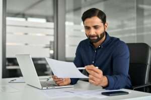 Busy Indian business man reading financial paper checking report in office.