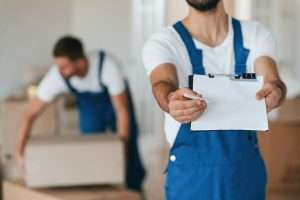 Close up view. Holding blank document to sign. Two moving service employees in a room