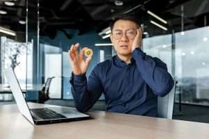 Dissatisfied and confused in depression asian financier investor, holding coin money crypto currency