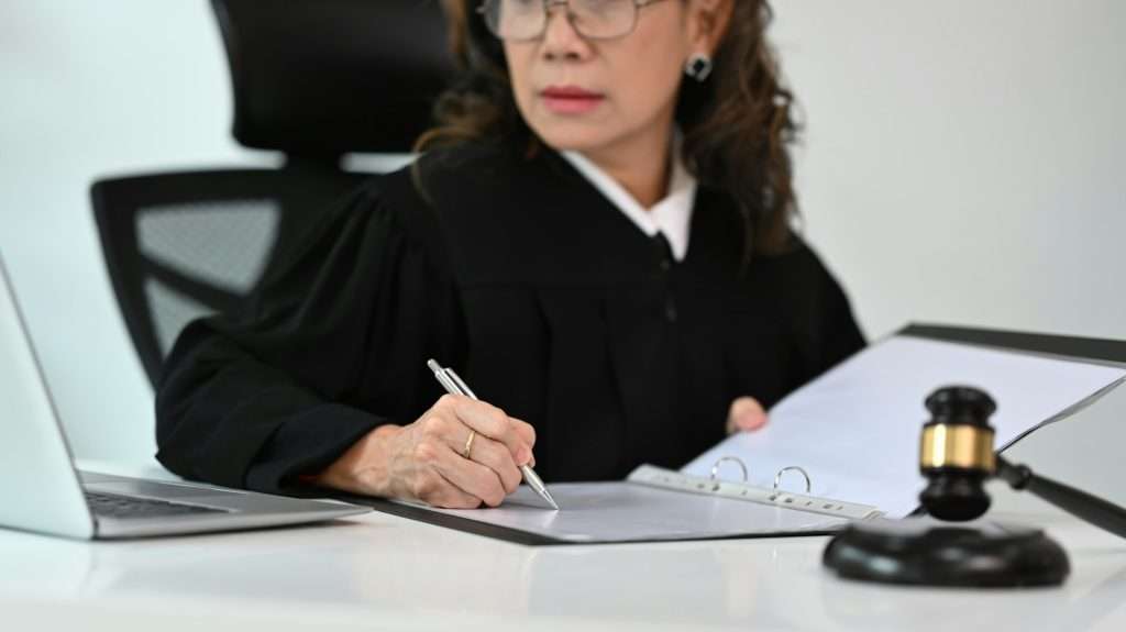 lawyer or attorney dressed in robe gown uniform sitting at table with gavel hammer.