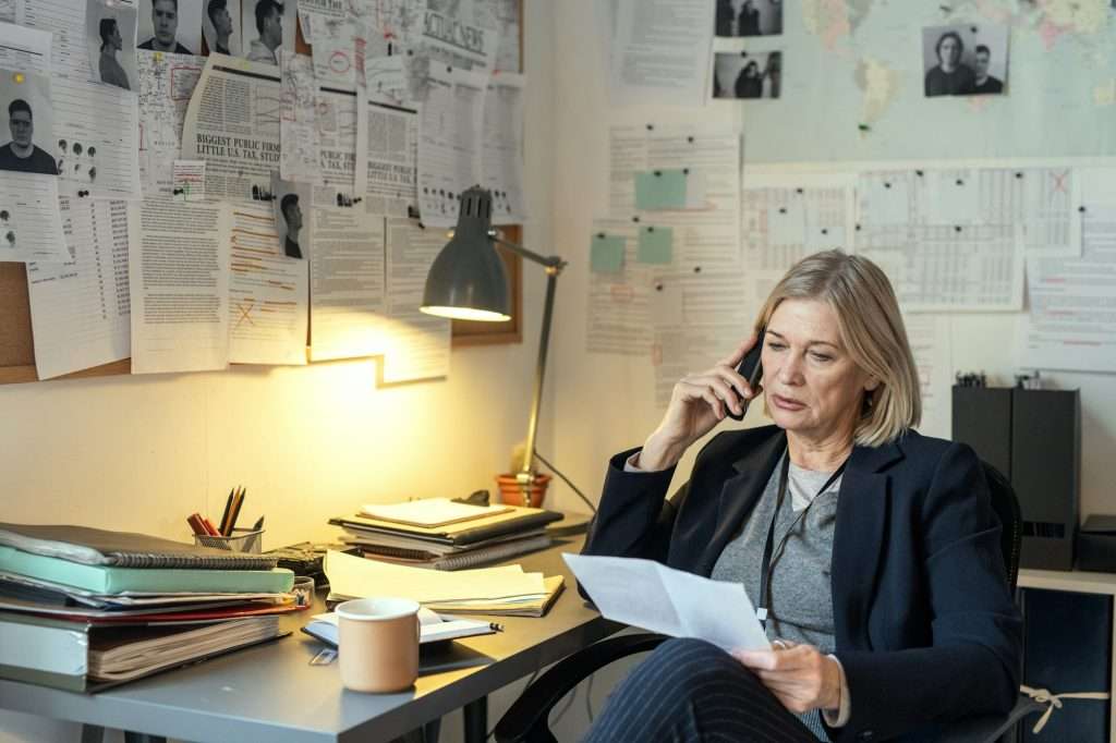Mature female investigator questioning witness on the phone by workplace