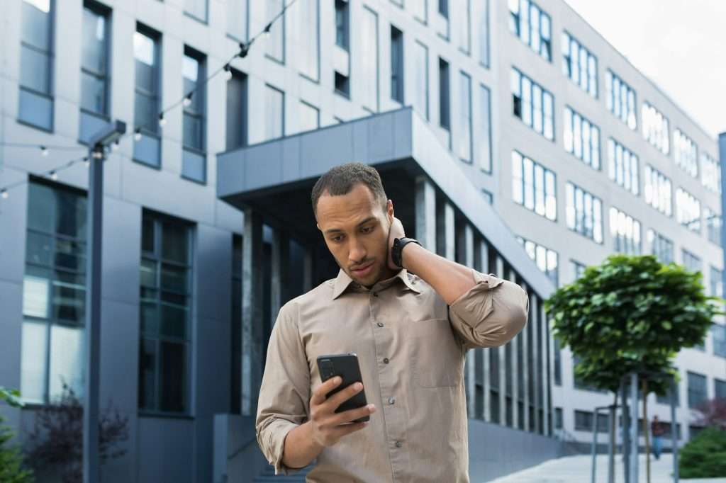 Pensive and excited african american worker outside office building reading bad news, man holding