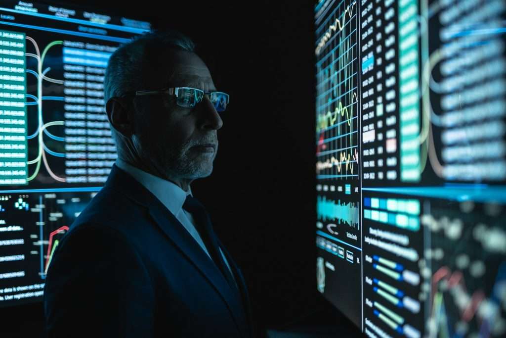 The businessman standing near the big screen in the dark room