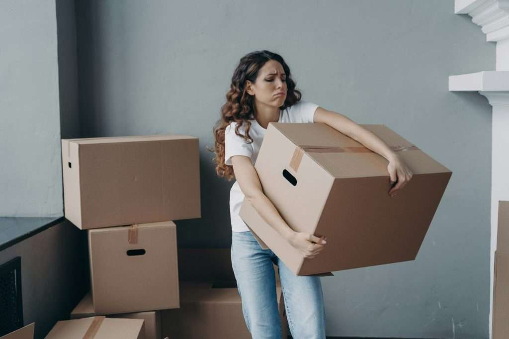 Tired female tenant carrying box with things leaving rented apartment. Eviction, hard relocation day