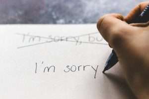 Woman’s hand writing a card that says I’m sorry apologizing