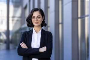 Portrait of a smiling young female lawyer standing outside the courthouse in a business suit, arms