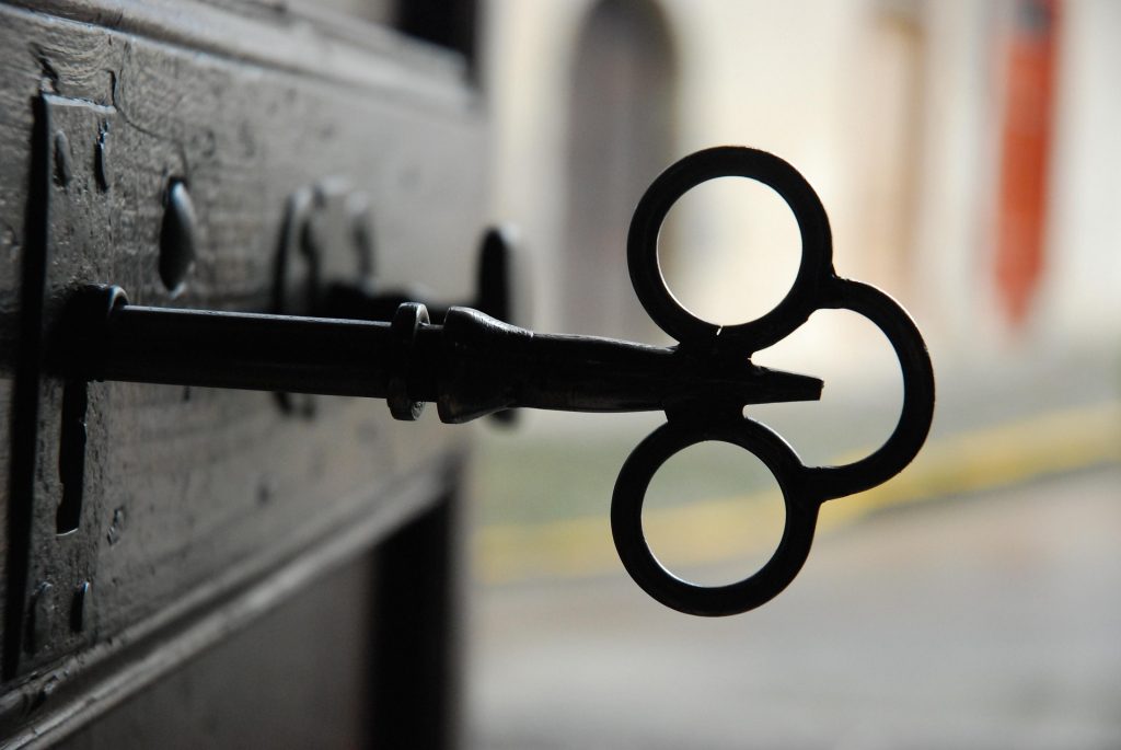 An old iron key in the lock of a dark wooden door, with a blurred street beyond