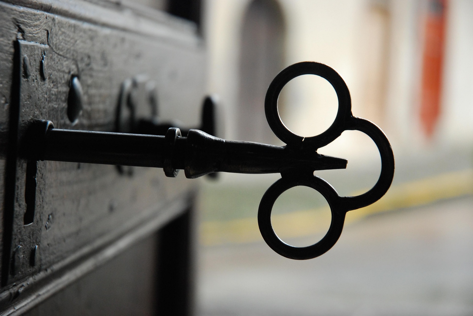 An old iron key in the lock of a dark wooden door, with a blurred street beyond