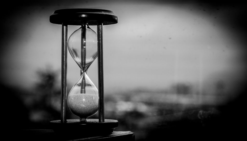 An hourglass with the sand running through it, in black and white, against a blurred window